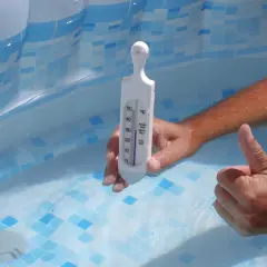 Ręka z termometrem w basenie, sprawdzająca temperaturę wody. Domowe sposoby na podgrzewanie wody w basenie mogą być skuteczne.