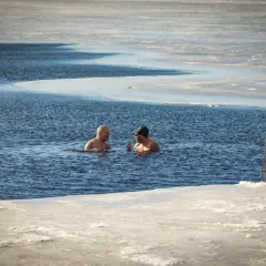 Dwóch mężczyzn rozmawia w wodzie, obok nich przerębel i drabinka.