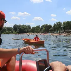 Ratownik wodny w łodzi obserwuje plażowiczów. W tle tłumy ludzi na plaży i w wodzie.