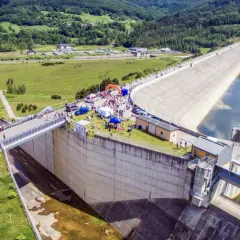 Wydarzenie sportowe przy zaporze w Świnnej Porębie. Tłum ludzi, namioty i pomarańczowa brama startowa na tle monumentalnej budowli.