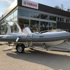 Szara łódź typu RIB na przyczepie przed budynkiem z logo Yamaha.