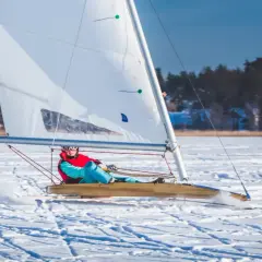 Osoba na bojery ślizga się po lodzie, żagiel łapie wiatr. To właśnie bojery co to za sport zimowy!