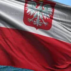 Flaga polska powiewa na wietrze, biało-czerwona z godłem orła.