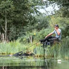 Wędkarz łowi rybę w siatce na tle zieleni.