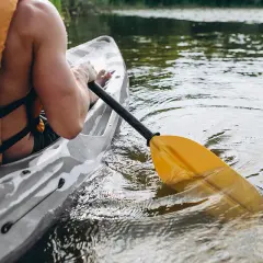 Spływ kajakowy rzeką Piławą. Wiosło zanurzone w wodzie, kajakarz w kamizelce ratunkowej.