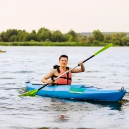 Uśmiechnięty mężczyzna w kamizelce ratunkowej pływa kajakiem po rzece. To dowód, że można pływać kajakiem po rzece i cieszyć się przygodą.