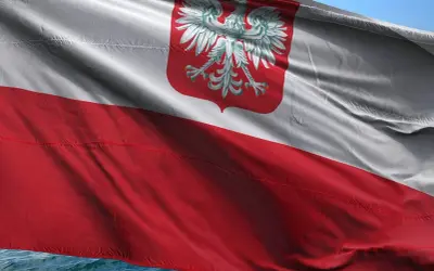 Flaga polska powiewa na wietrze, biało-czerwona z godłem orła.