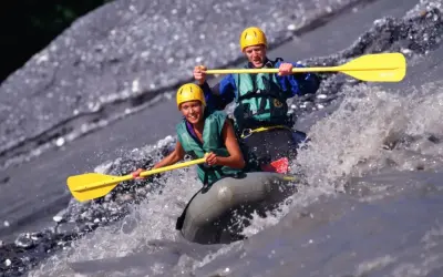 Dwóch uśmiechniętych ludzi w kaskach i kamizelkach płynie pontonem po rwącej rzece. To właśnie rafting – ekscytująca przygoda!