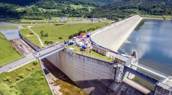 Wydarzenie sportowe przy zaporze w Świnnej Porębie. Tłum ludzi, namioty i pomarańczowa brama startowa na tle monumentalnej budowli.