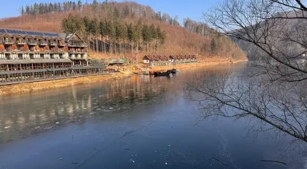 Zamarznięte Jezioro Bystrzyckie z hotelem i domkami w tle, otoczone lasem.