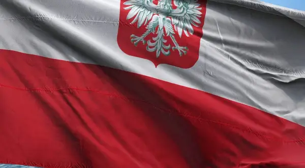 Flaga polska powiewa na wietrze, biało-czerwona z godłem orła.