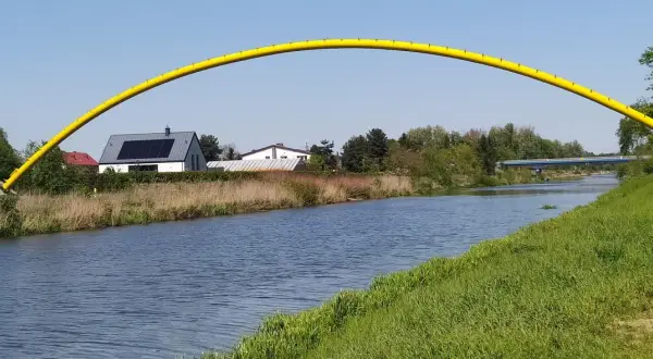 Żółty łuk mostu nad kanałem żerańskim, z domami i zielenią w tle.