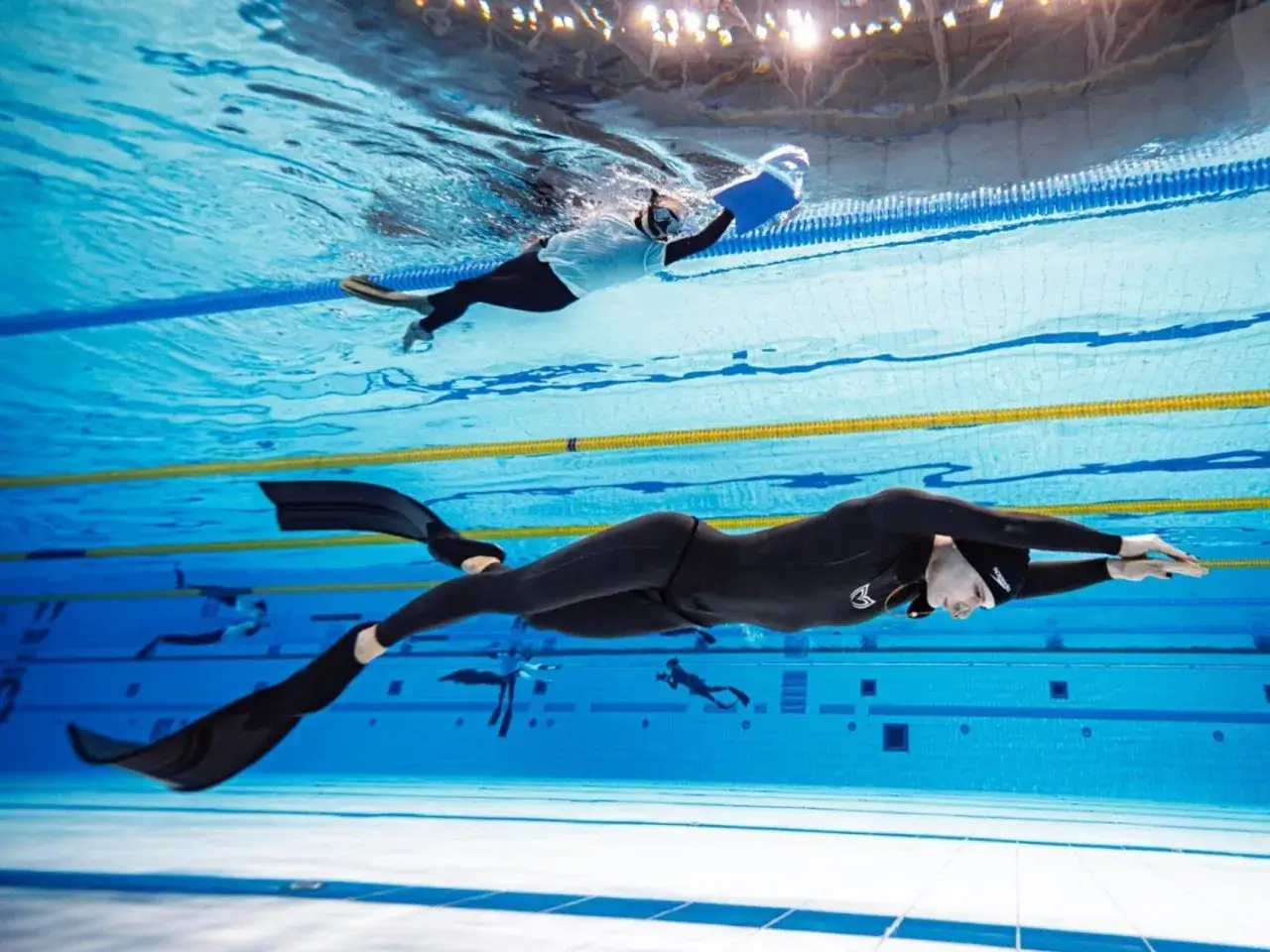Pływak w czarnym stroju z płetwami dąży do pobicia freediving rekord. Inny zawodnik płynie wyżej.