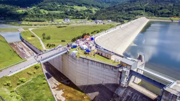 Wydarzenie sportowe przy zaporze w Świnnej Porębie. Tłum ludzi, namioty i pomarańczowa brama startowa na tle monumentalnej budowli.