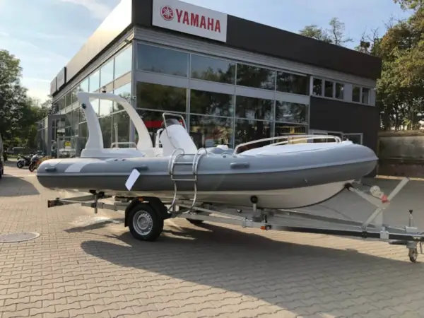 Szara łódź typu RIB na przyczepie przed budynkiem z logo Yamaha.