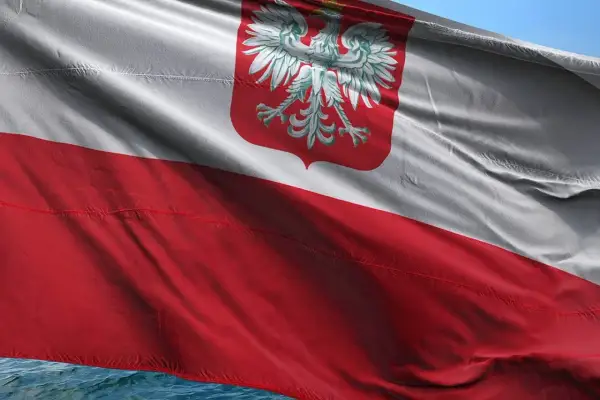 Flaga polska powiewa na wietrze, biało-czerwona z godłem orła.