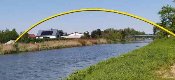 Żółty łuk mostu nad kanałem żerańskim, z domami i zielenią w tle.